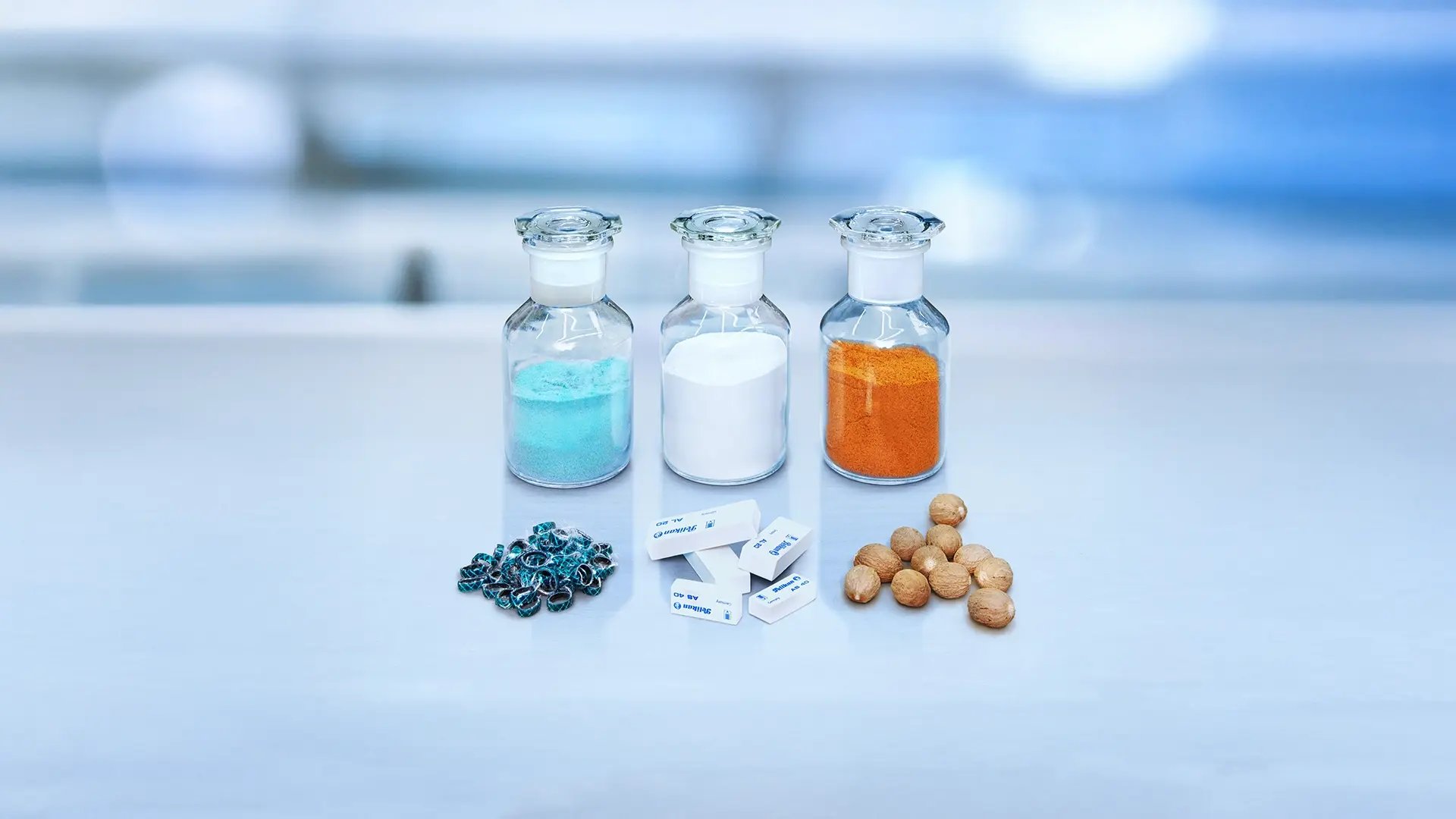 Drei Glasfläschchen mit türkisem, weißem und orangefarbenem Pulver, davor Reste von einem Gartenschlauch, Radiergummis und Muskatnüsse.