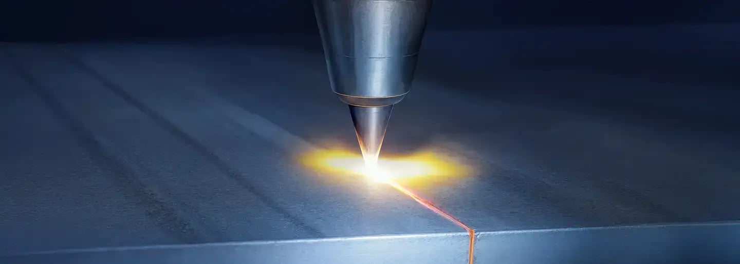 Eine Nahaufnahme einer Laserschneidmaschine, die ein helles gelbes Licht ausstrahlt, während sie präzise durch ein Metallblech schneidet und dabei eine leuchtende Linie entlang der Oberfläche erzeugt.